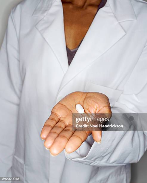 mid section shot of a woman wearing a lab coat holding a pill in her hand - lab coat stock-fotos und bilder