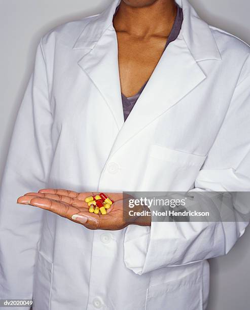 mid section of a woman in a lab coat holding pills in her hand - lab coat stock-fotos und bilder