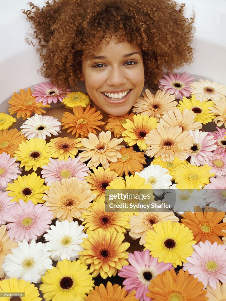 Young Woman With Curly Hair Lies in a Bath of Multicolored, Floating Flowers