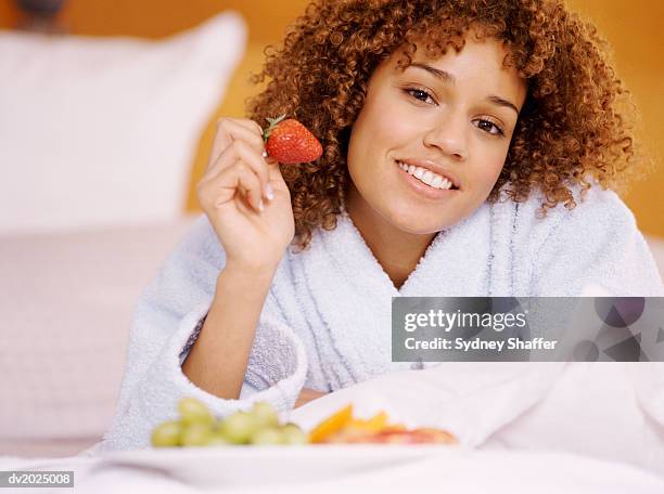 portrait of a young woman in a dressing gown holding a fresh strawberry - dressing up ストックフォトと画像