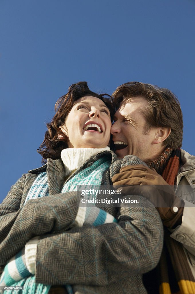 Low Angle View of a Mature Couple in Winter Clothing Embracing and Laughing