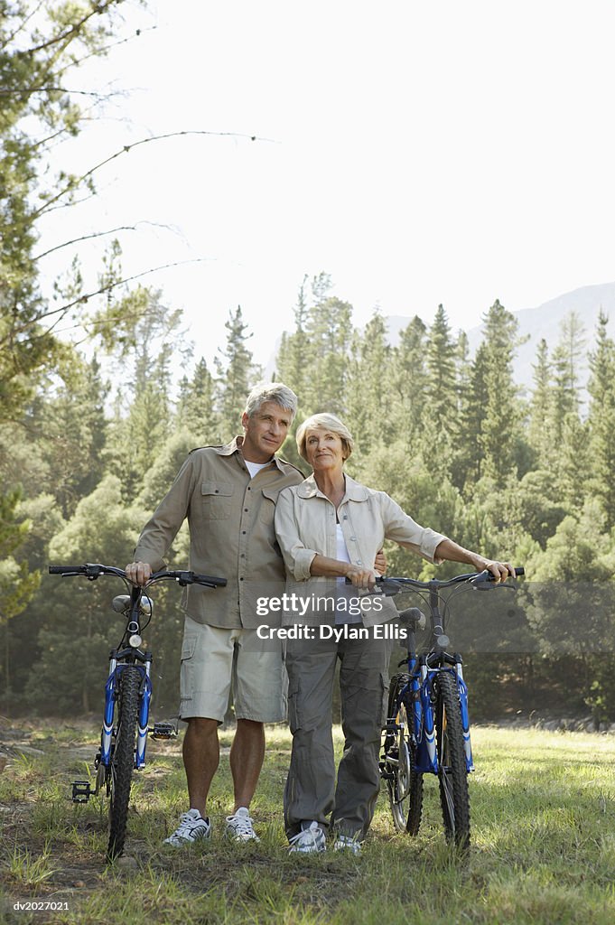 Senior Couple Standing Side by Side With Their Bikes With Woodland in the Background
