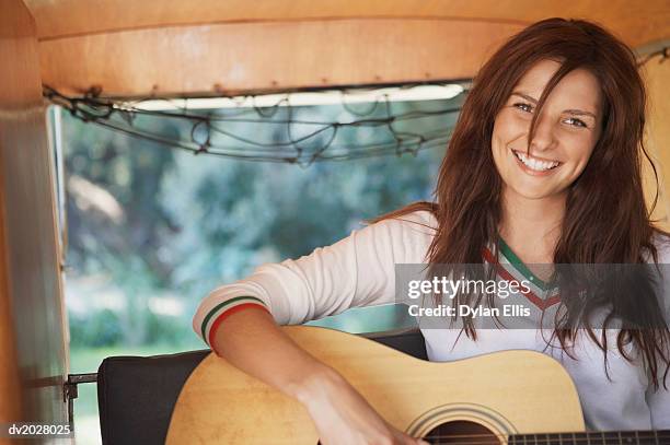 young woman playing an acoustic guitar on the back seat of a motor home - ellis stock-fotos und bilder