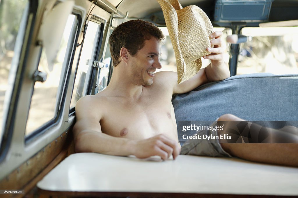 Smiling, Young Man Sitting With His Feet Up in a Motor Home and Holding a Straw Hat