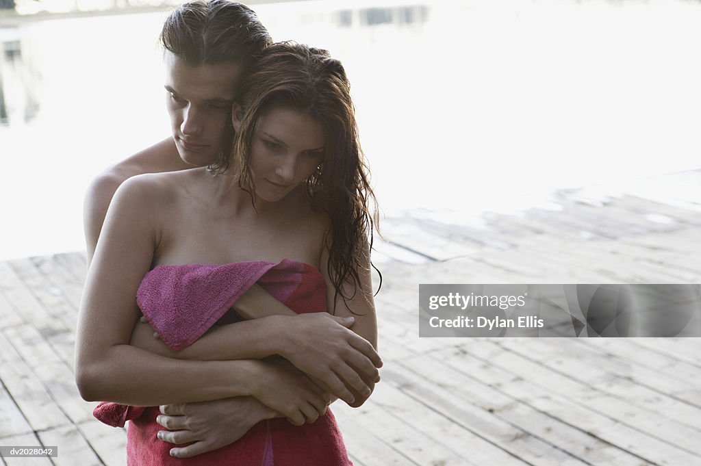 Couple Wrapped in Towels Stand on Decking, Embracing