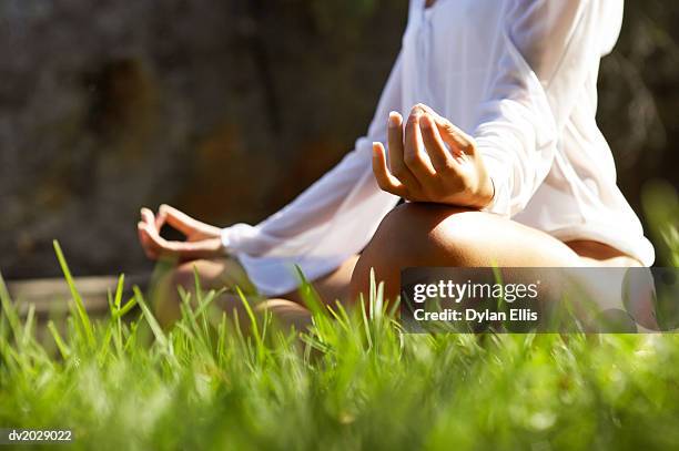 low section view of a young woman sitting in the lotus position on the grass - ellis stock-fotos und bilder