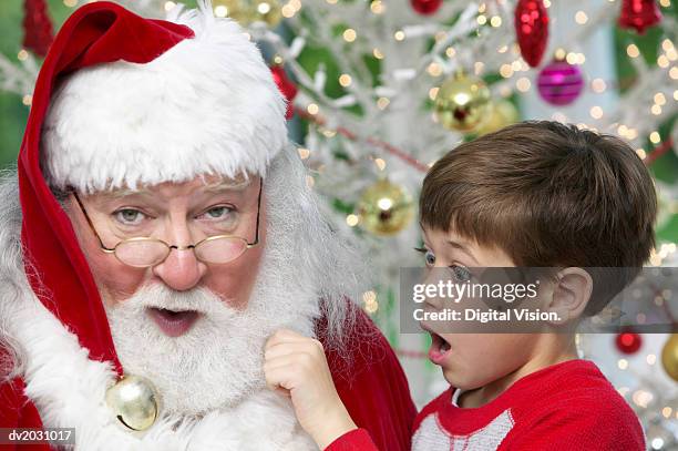 young boy pulls santa's beard, gasping with surprise - beard stock pictures, royalty-free photos & images