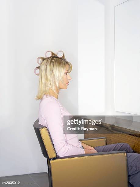 woman in curlers sitting in a chair at a hair salon - hair curlers stockfoto's en -beelden