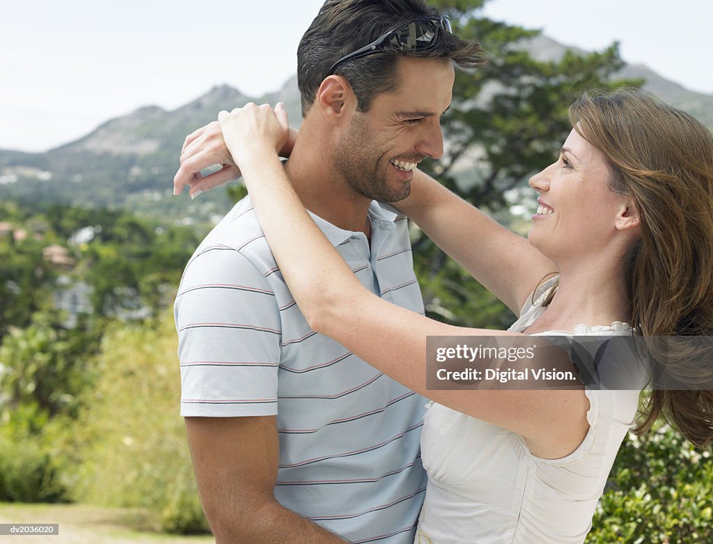 Smiling Couple Standing Face to Face in the Countryside With Their Arms Around Each Other