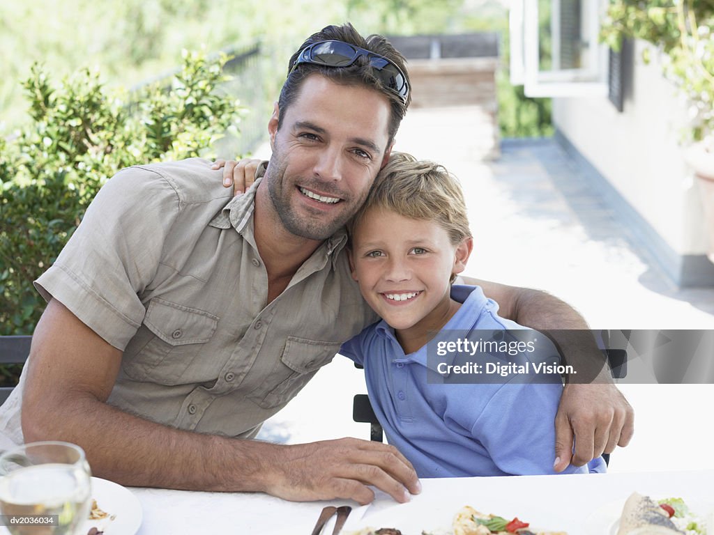 Portrait of a Smiling Father Sitting With His Son at a Dinner Table Outdoors