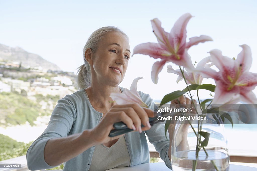 Senior Woman Sitting at a Table and Pruning Cut Flowers in a Vase