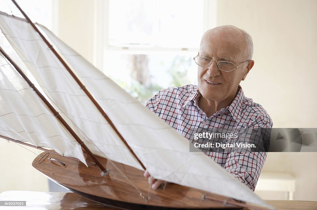 Senior Man Sitting at a Table and Examining a Model Yacht