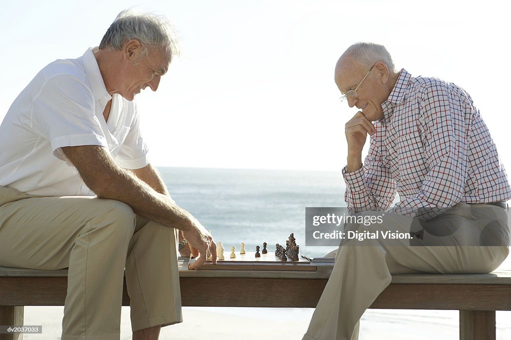 Two Senior Men Playing Chess, with the Sea in the Background