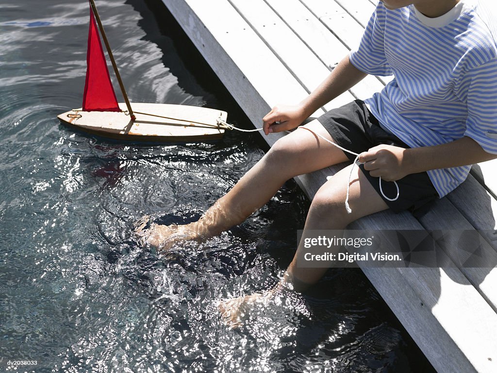 Low Section of a Young Boy Sitting on a Promenade Playing With a Toy Boat
