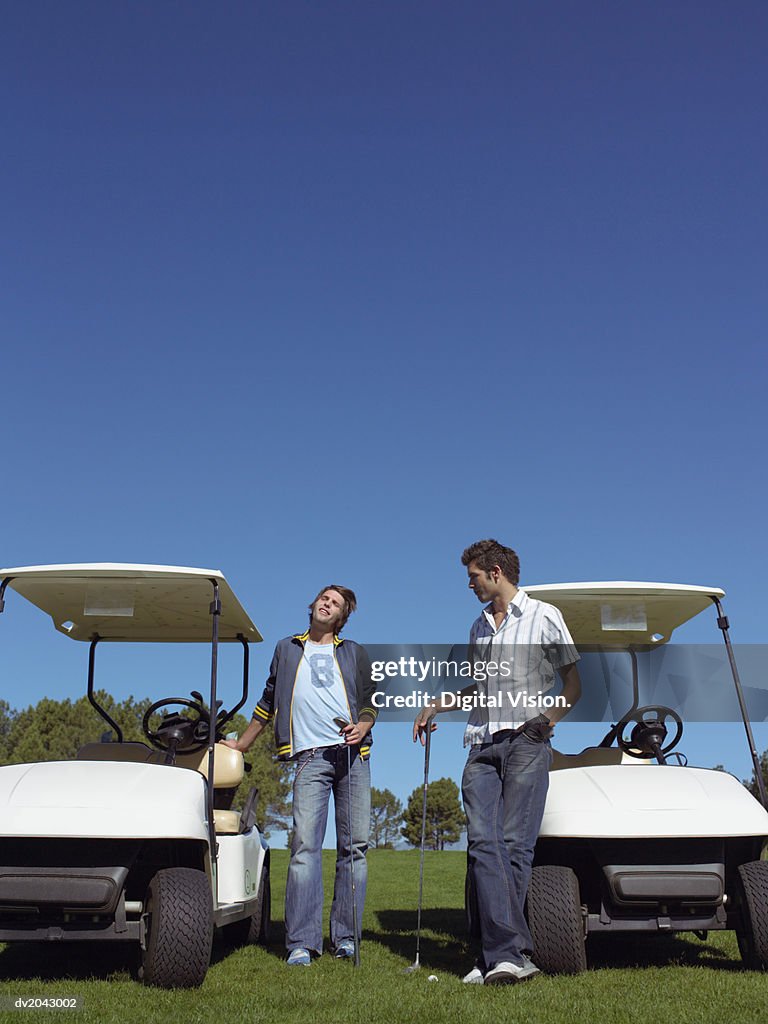 Two Young Men Standing by Golf Buggies and Holding Golf Clubs