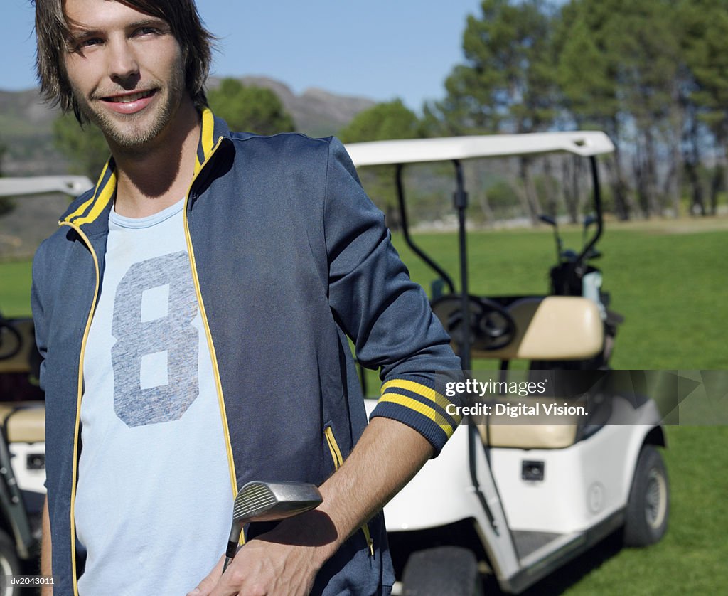 Portrait of a Young Man Holding a Golf Club with a Golf Buggy in the Background