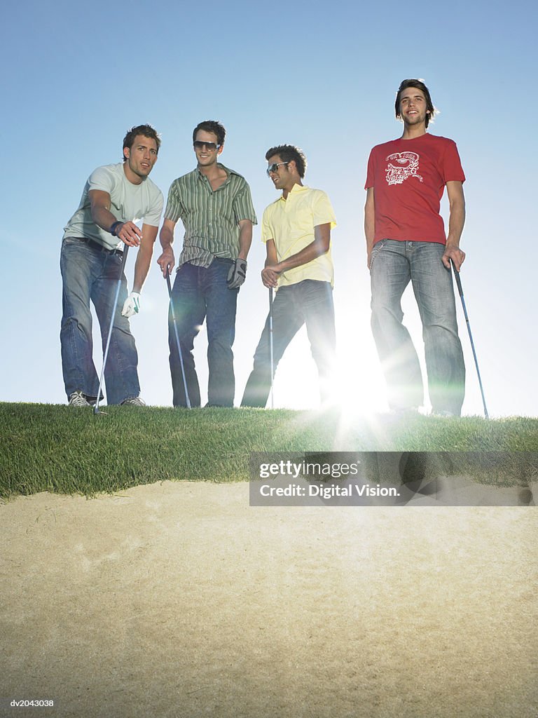 Four Young Men Standing at the Edge of a Sand Bunker Holding Golf Clubs