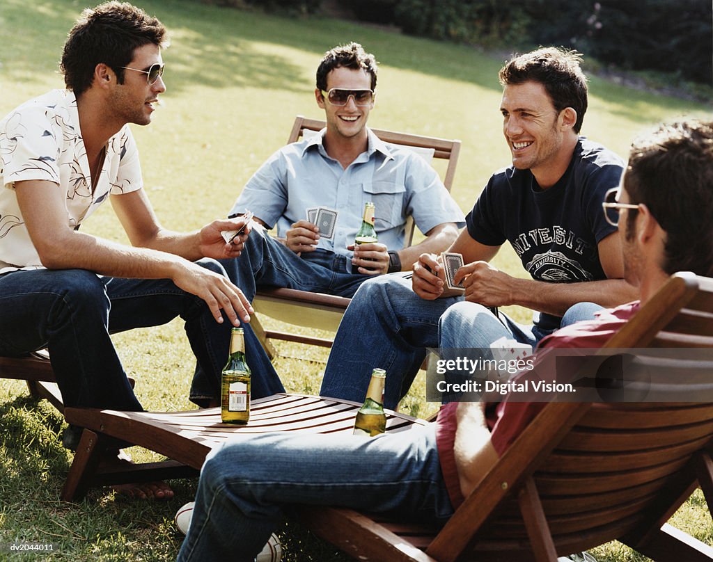 Group of Men Sitting on Sunloungers Playing Cards and Drinking Beer