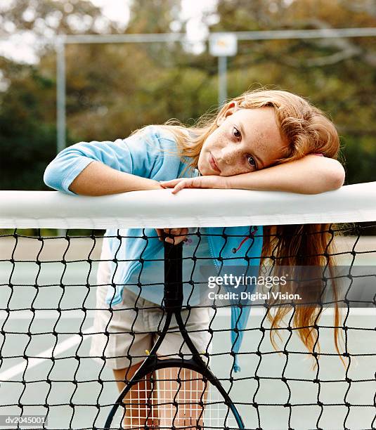 portrait of a young girl leaning on a net in a tennis court - tennis court stock pictures, royalty-free photos & images