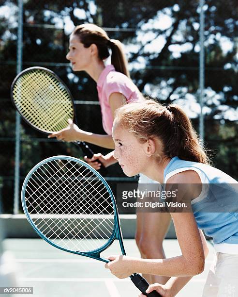 profile of a young girl and her mother standing on a tennis court holding their raquets with anticipation - tennis court stock pictures, royalty-free photos & images