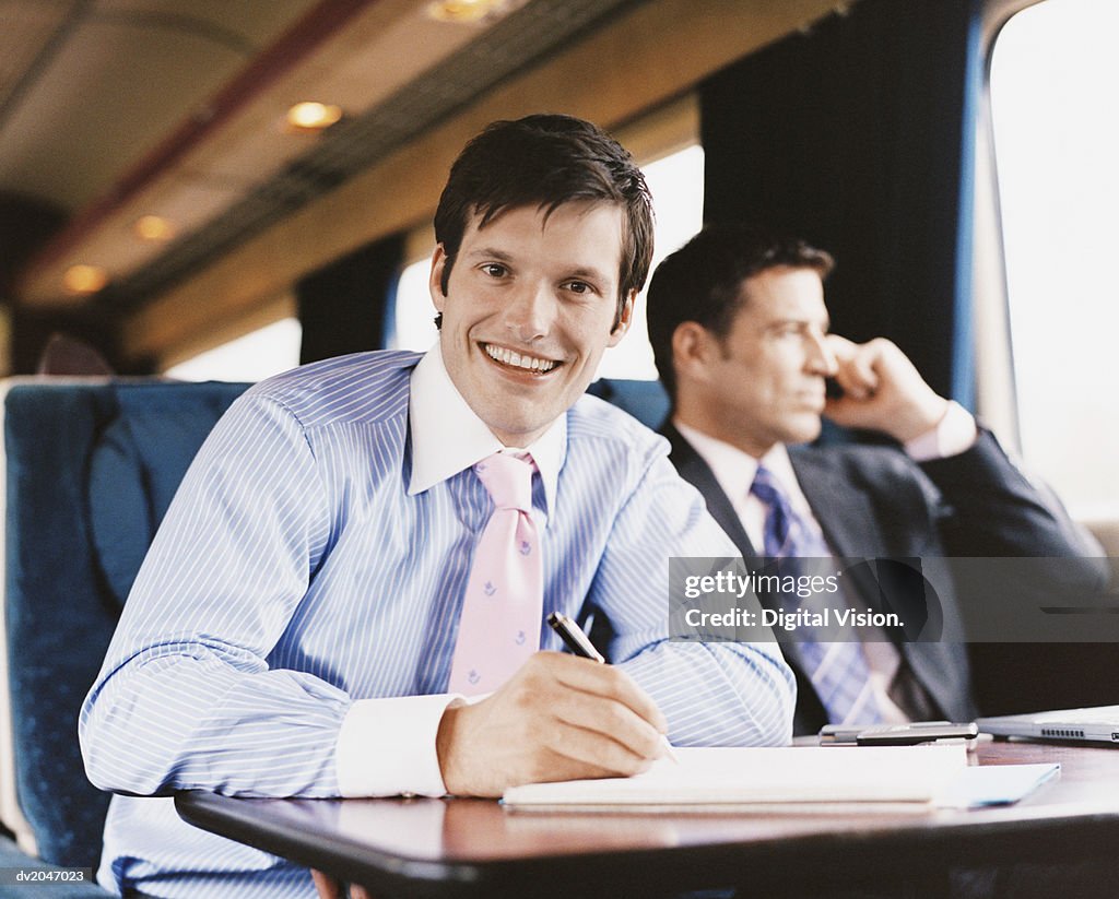 Smiling Businessman Writing in a Document on a Passenger Train