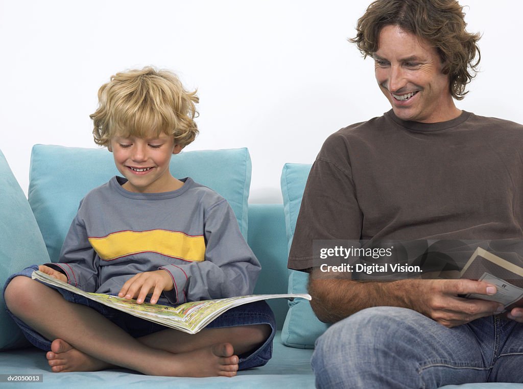 Father and Son Sitting on a Sofa Reading Books