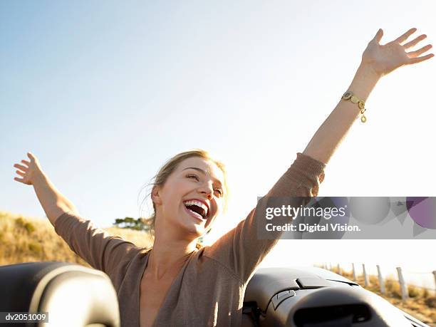 young woman sits in the back of a convertible, her arms in the air, laughing with joy - air vehicle 個照片及圖片檔