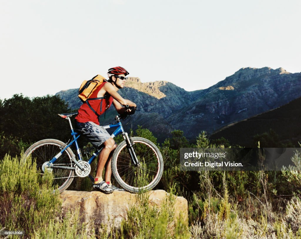 Young Man Sitting on a Bike and Looking at a View of Mountains