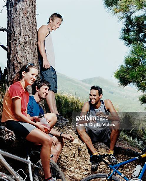 four people resting by a tree trunk with their mountain bikes - tree people stock-fotos und bilder