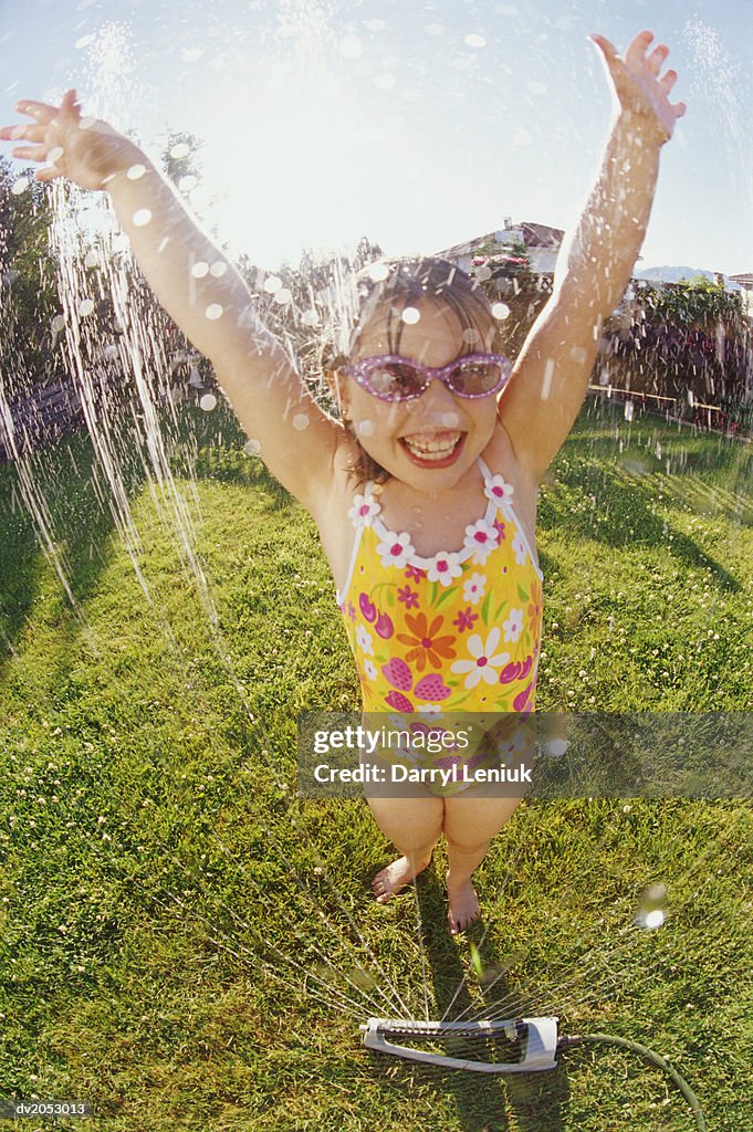 Young Girl Wearing a Swimming Costume, Being Sprayed with Water From a Garden Sprinkler