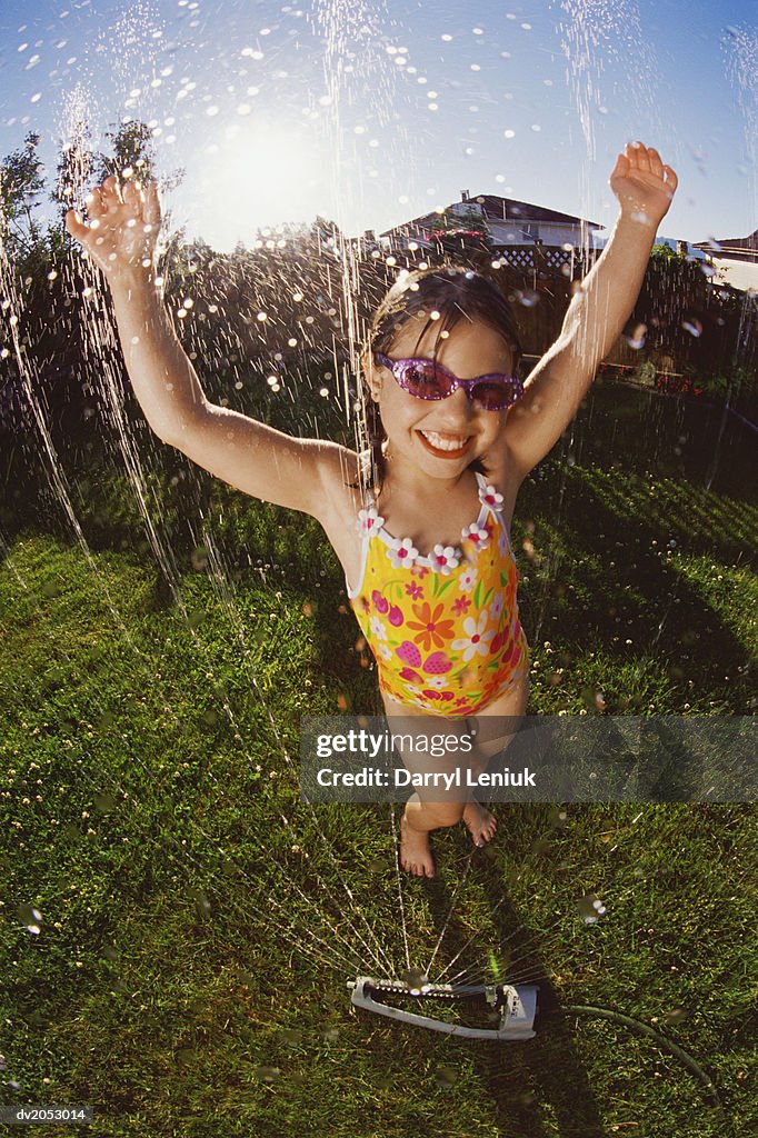 Gel Effect Shot of a Young Girl Wearing a Swimming Costume, Being Sprayed with Water From a Garden Sprinkler