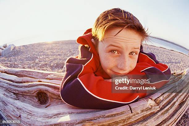 fisheye lens shot of a young boy leaning against a log on a pebbled beach - fish eye lens stockfoto's en -beelden