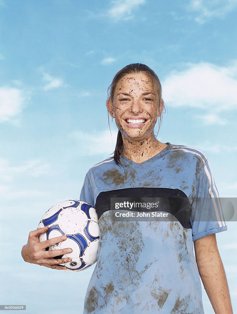 Portrait of a Female Footballer Covered in Mud and Holding a Football
