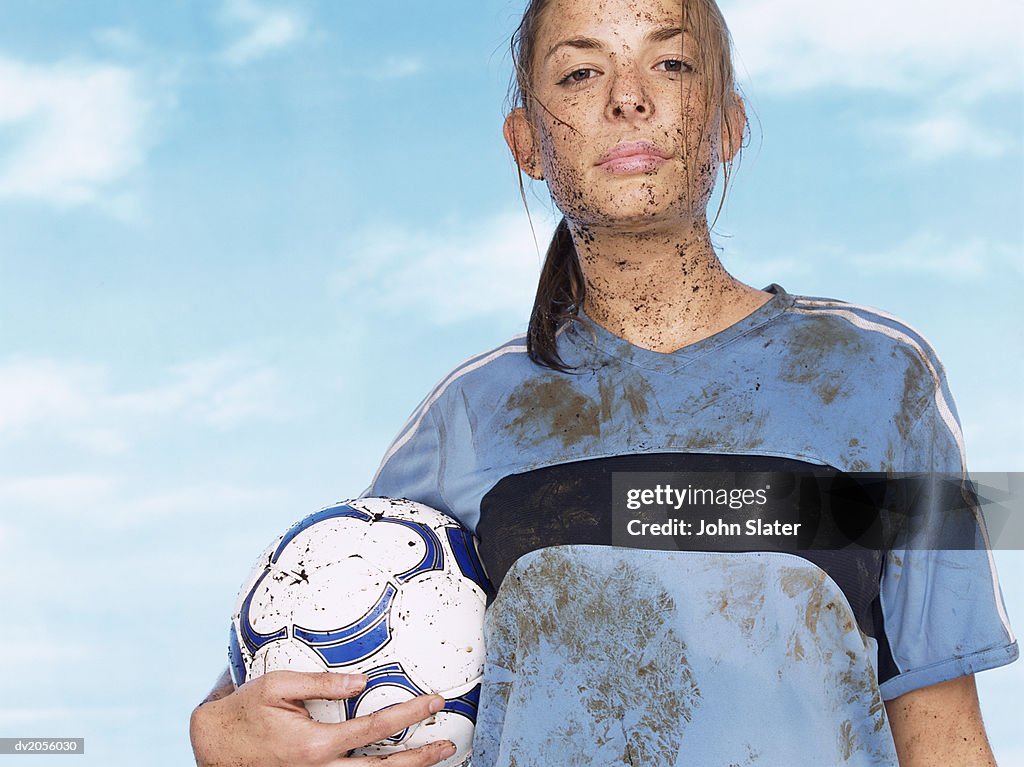 Female Footballer Splattered with Mud and Holding a Football