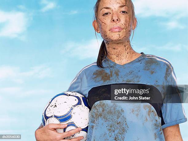 female footballer splattered with mud and holding a football - mud splatter stock pictures, royalty-free photos & images