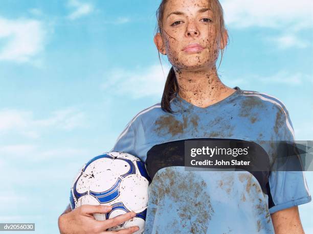 female footballer splattered with mud and holding a football - mud splatter stock pictures, royalty-free photos & images