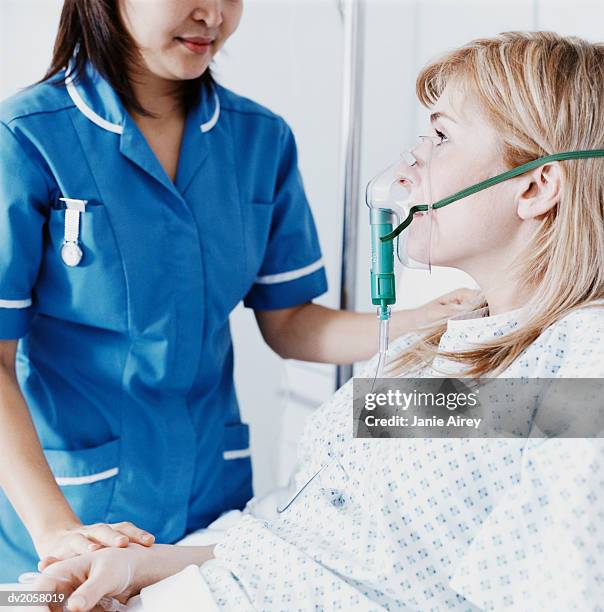 nurse stands by a female patient on a ventilator, holding her hand - hospital ventilator stock pictures, royalty-free photos & images