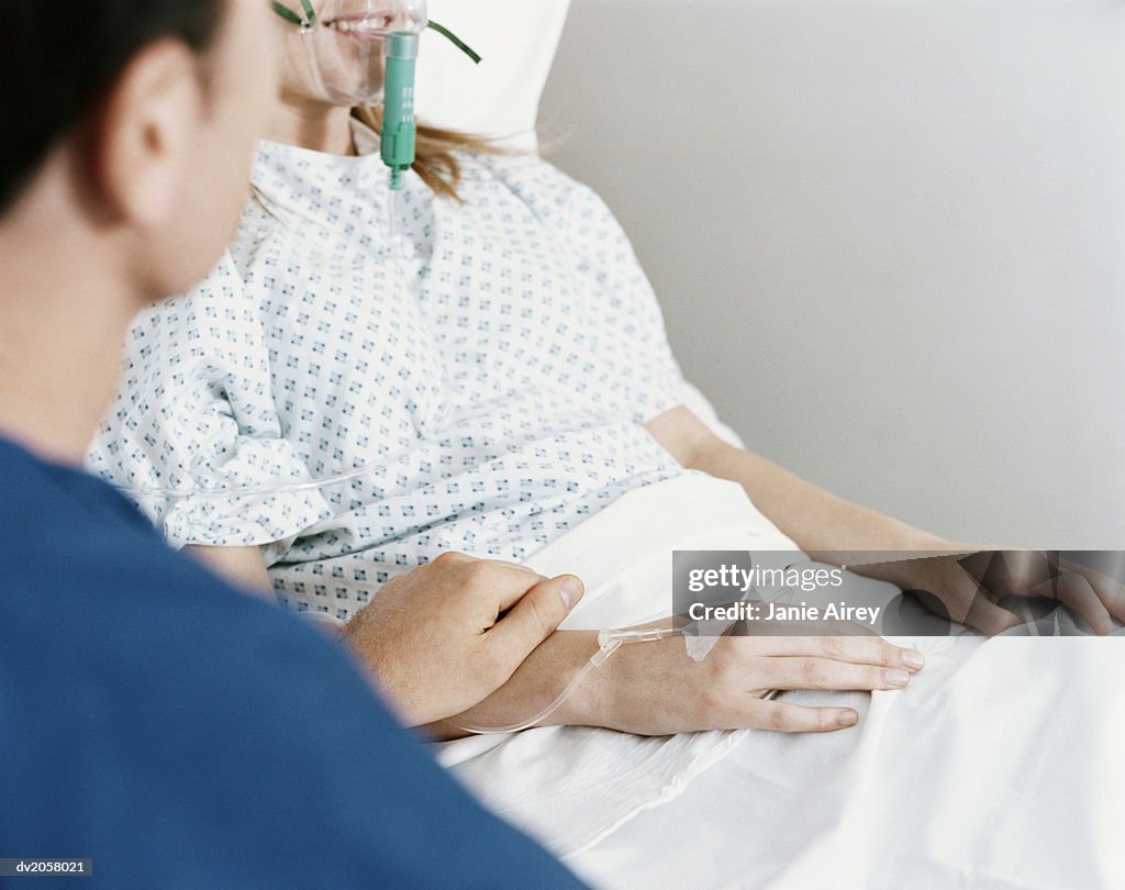 Mid Section of a Woman Lying in a Hospital Bed With a Ventilator and Intravenous Drip, a Man Holding Her Hand