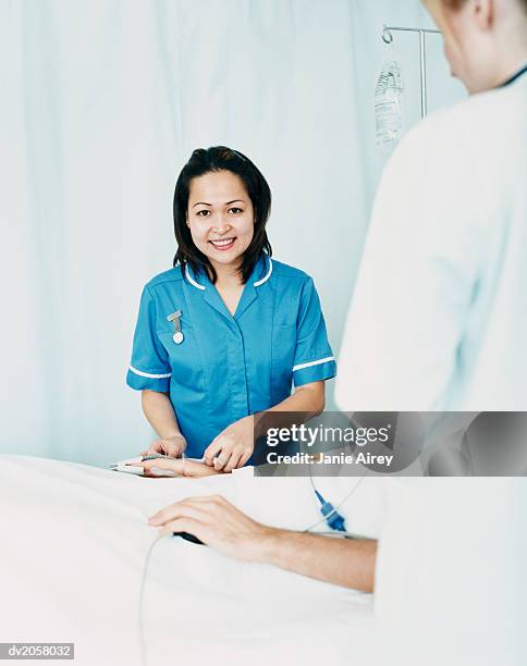 smiling nurse stands by a patient's bed, adjusting the intravenous drip - rapporto medico paziente foto e immagini stock