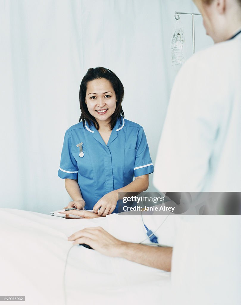 Smiling Nurse Stands by a Patient's Bed, Adjusting the Intravenous Drip