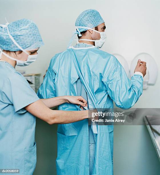 female surgeon helping male surgeon with his operating robe - get dressed male stock-fotos und bilder