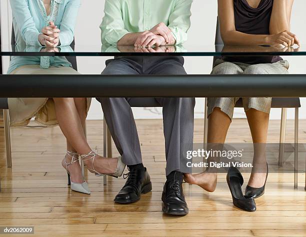 low section view of two businesswomen touching the feet of a businessman under a table - high and low stockfoto's en -beelden