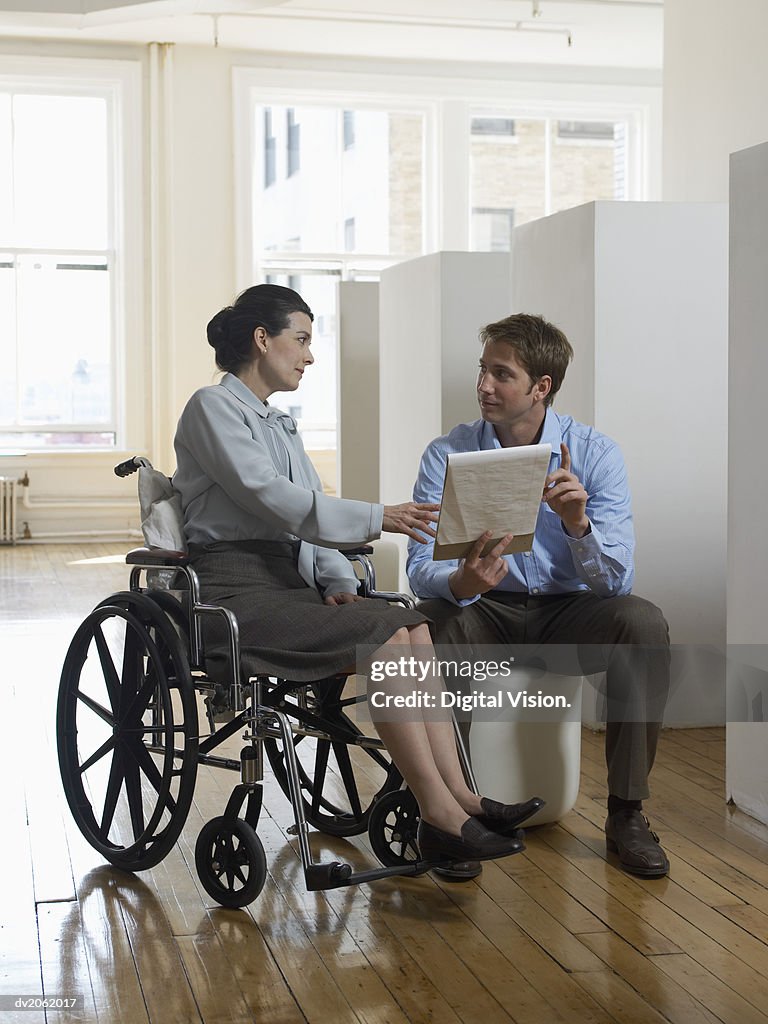 Businessman Discussing a Document With a Businesswoman Sitting in a Wheelchair