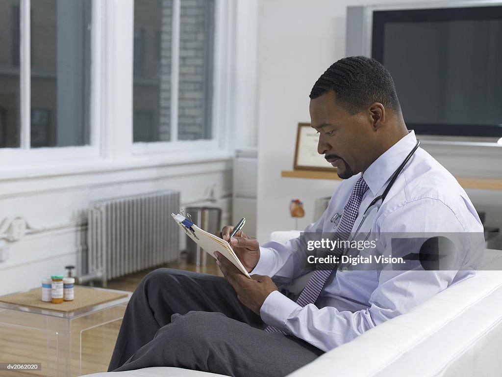 Physician Sitting on a Sofa in a Living Room and Writing in a Document