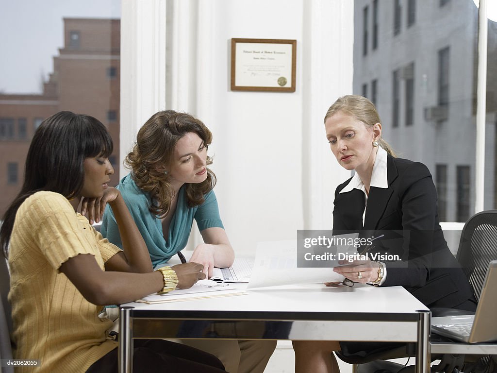Doctor Explaining a Document to Two Women Sitting at Her Desk in Her Clinic