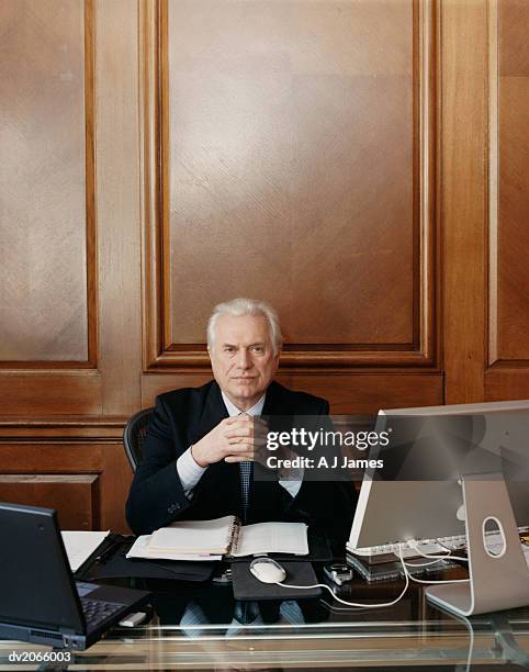 portrait of a serious looking ceo sitting at his desk - ceo desk stock-fotos und bilder