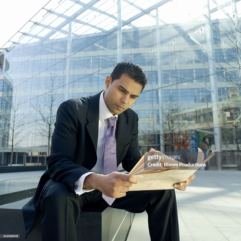 Businessman Sits on a Bench Reading a Newspaper