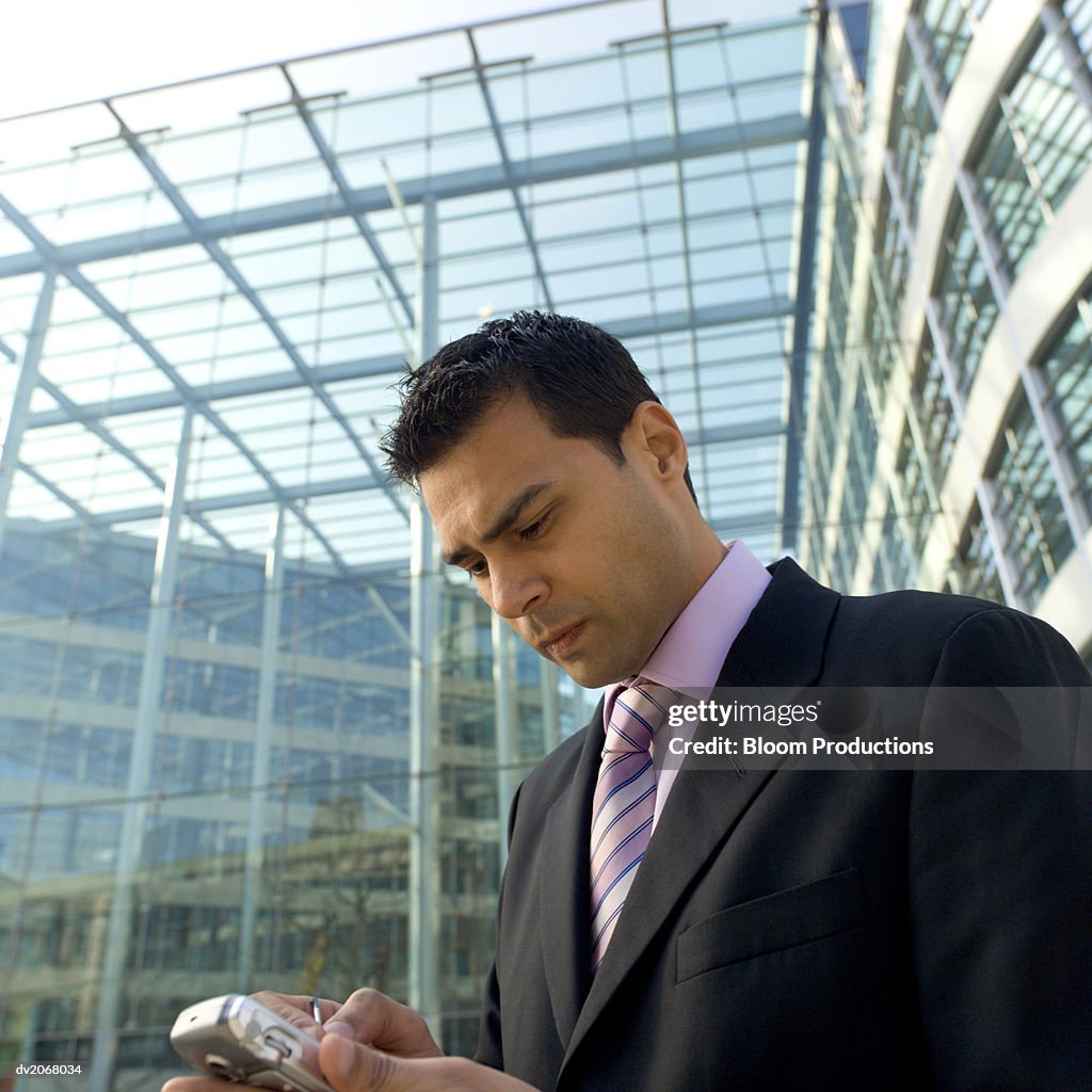 Businessman Stands Outside a Glass Building Using a Handheld PC