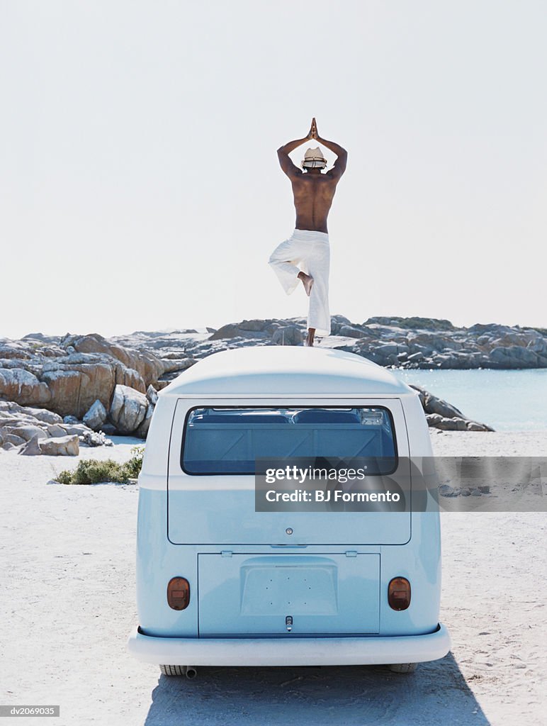 Man Standing on the Roof of a Camping Van Practising Yoga