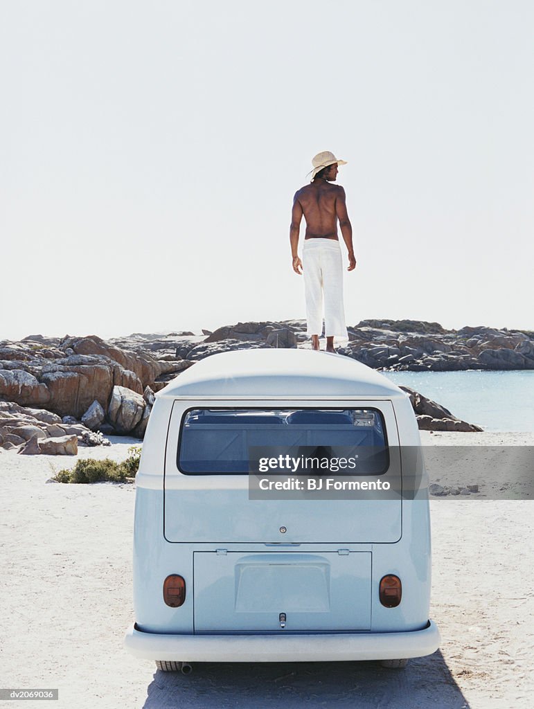 Man Standing on the Roof of a Camping Van Looking at View